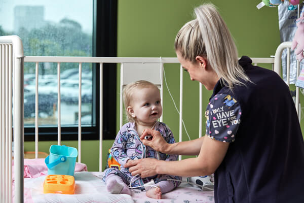 A nurse cares for a smiling toddler in a cot