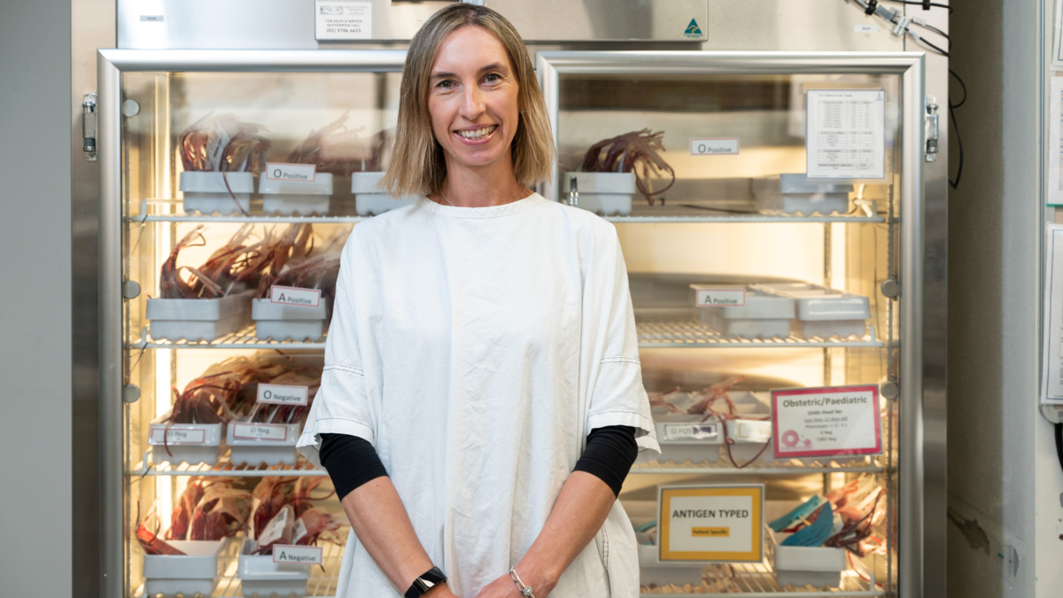 A pathologist stands in front of a fridge storing blood products. 