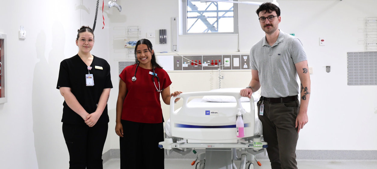 Graduates standing together in a clinical room, showcasing collaboration across disciplines in the hospital’s care team. From left to right: Isabella (Graduate Nurse), Olivia (Medical Intern) and Nate (Graduate Social Worker)