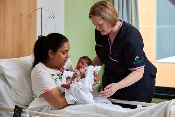 Mother and baby with a midwife A new mother holds her baby while a midwife watches on for support