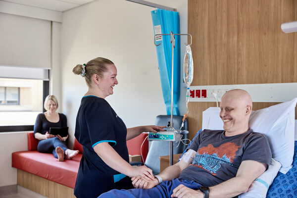 Staying overnight A patient is cared for by a nurse at the bedside while his carer reads by a window