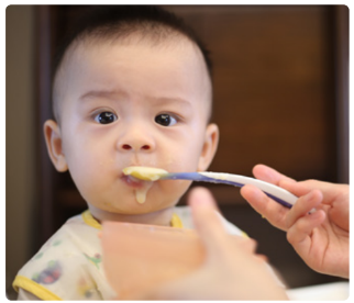 A baby wearing a bib is being fed by a adult using a spoon