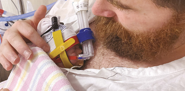 Close-up of a man with his newborn baby in an upright position on his bare chest in a hospital setting.