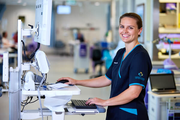 A nurse at a computer smiles at the camera