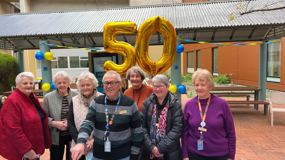 Group of Auxiliary volunteers celebrating 50 years with a cake.