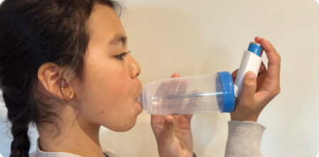 Young girl taking an asthma puffer using a spacer.