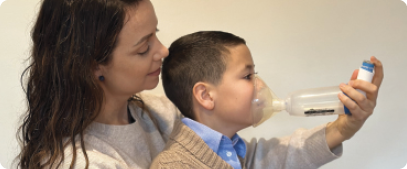Image of a woman administering a puffer to their child using a mask and spacer.