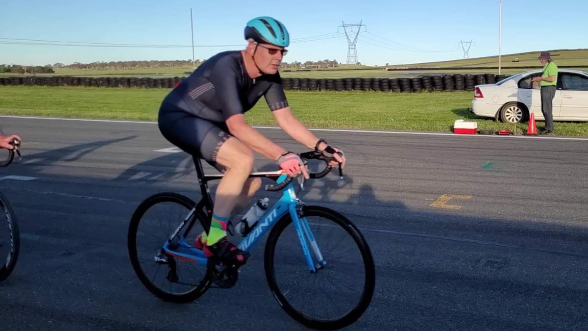 A man is riding a blue bike. He is wearing a navy cycling suit and blue helmet. He is racing around a track.