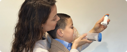 Image of a woman shaking a puffer before administering the puffer to their child again using a mask and spacer.