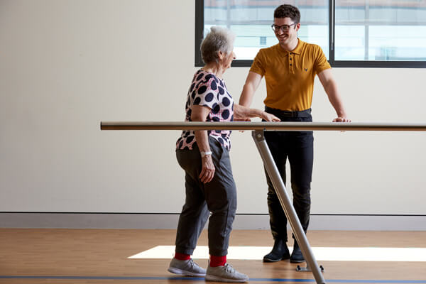 A woman walks with an aid under the care of a physiotherapist