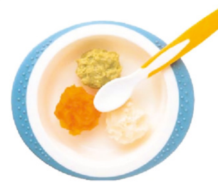A white bowl with a blue rim containing three dollops of pureed food—green, orange, and white. A white spoon with a yellow handle rests inside the bowl, which has raised dots on the rim for grip.