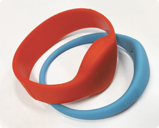 Two bracelets used for accessing the facility, the bracelets are made of rubber or plastic and are a similar size to a watch. One is red, the other is teal.